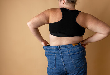 Close-up of belly and back rolls of plus size woman against beige background