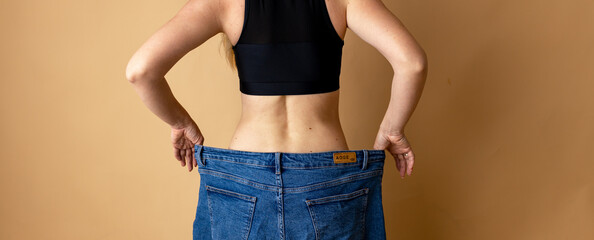 Diet concept and weight loss. Woman in oversize jeans on beige background