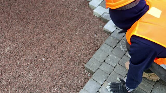 Worker Installing Pavement Blocks, A worker in orange safety gear carefully places interlocking pavement blocks on a freshly prepared base layer.