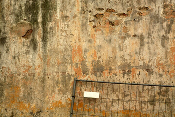 Grungy metal fence against dirty weathered cement wall.