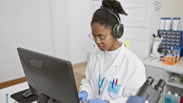Focused black woman scientist analyzing data on computer in modern laboratory indoor setting.