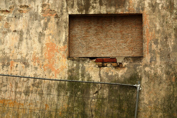 Naklejka premium Grungy metal fence against dirty weathered cement wall.