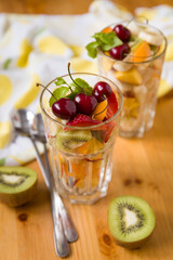Healthy snack with chopped fruits and berries on the table. Tangerine, kiwi, banana, strawberries, mango, cherries and mint leaves in transparent cup