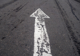 white painted pointing arrow on asphalt road with wet tyres tracks.