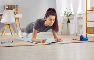 Smiling woman doing plank sport exercise, workout at home. She is engaged in fitness routine, demonstrating dedication to gym training and overall health. Providing healthy and active lifestyle.