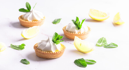 Aromatic homemade lemon tartlets with cream and mint leaves on white marble table close up.
