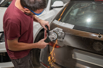 Mechanic using a grinder on a car tailgate to repair it
