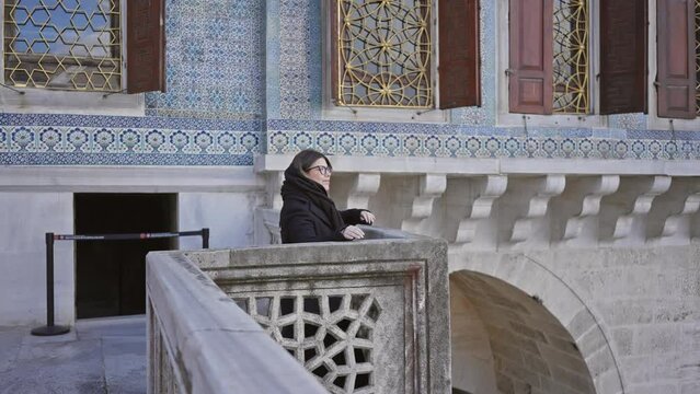 A thoughtful woman leans on a balustrade at the tiled topkapi palace in istanbul, expressing tranquility and historical ambiance.