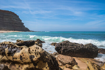 Landscape with rocks and breaking sea wave and cliff on the horizon at Calada beach, Ericeira...