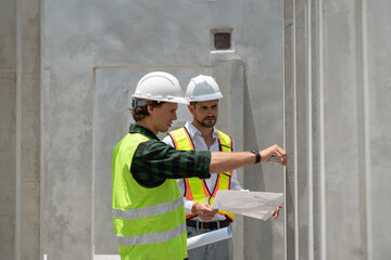 Two men in construction gear are looking at a wall