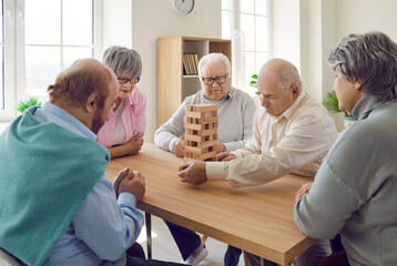 Group of senior men and women playing together with wooden building blocks for dementia therapy in...