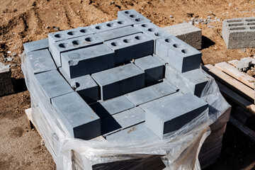 Stack of grey concrete blocks neatly stacked on construction site, wrapped in plastic for protection. Part of building materials for urban development and foundation preparation