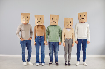 Diverse team wears paper bags on their heads, each adorned with a drawn sad face. This creative...