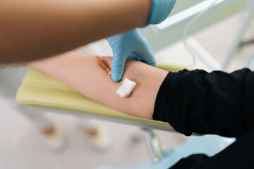 Top view of unrecognizable nurse giving intravenous infusion to female patient in clinic. Medical worker in uniform inserting IV line needle in vein of woman at hospital. Medicine, vitamin therapy.