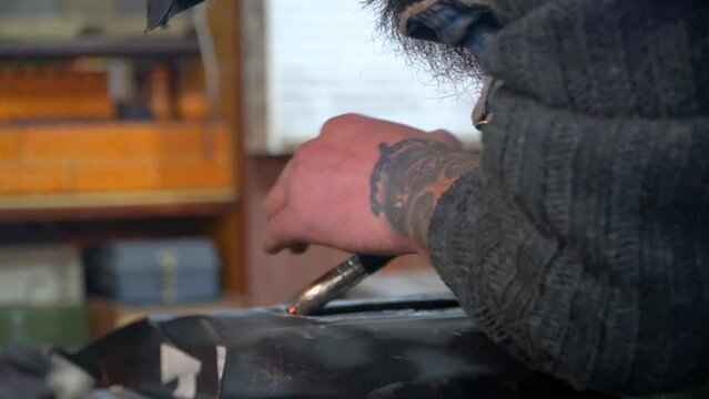 Close-up hands of male master without gloves in welding process on workshop background.Life hack how to make smooth movements to weld metal parts. Techniques instructions for using welding machine