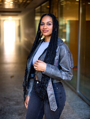 young smiling black female with afro braids is staying in a passage with a light in the background 