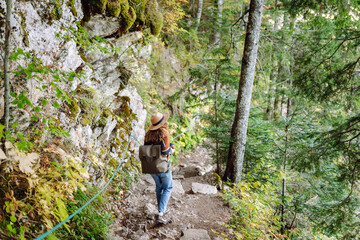 Young female traveler with backpack standing in forest with tall coniferous trees, enjoying nature. Weekend, tourism. 
