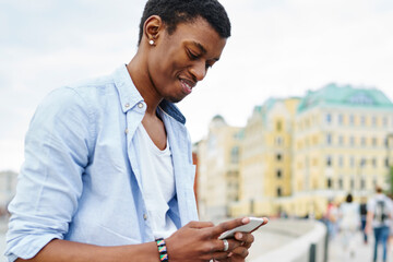 Positive african american hipster blogger chatting online in social networks on modern smartphone...