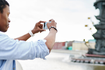 Side view of african american young man tourist shooting video on modern smartphone using 4G...