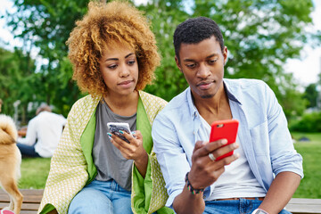Dark skinned young man and woman chatting online in social networks on modern smartphones using 4G...