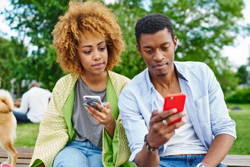 Dark skinned young man and woman chatting online in social networks on modern smartphones using 4G internet.African american male and female bloggers updating app on telephone devices