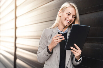 Cheerful business woman smiling at her tablet while walking outside.