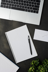 Black office desk table with blank notebook, laptop and other office supplies. Top view with copy space.