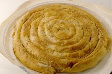 A photo of a cooked tasty twisted cheese pie in the shape of a roll  