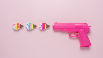 Pink handgun on pink pastel background with ice cream decor. Minimal concept.