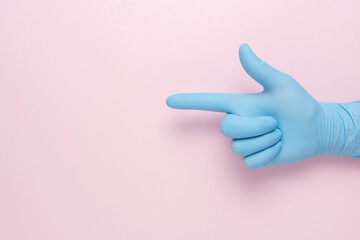 Hand in the blue glove depicts the gesture of a handgun on pink background. Minimal flat lay...