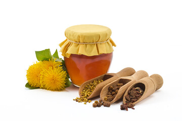A jar of honey with fabric lid, pollen granules, beebread, and dandelion flowers