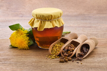 A jar of honey with fabric lid, pollen granules, beebread, and dandelion flowers