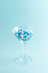 Martini glass full of colorful pills on blue background. Creative composition.