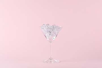 Martini cocktail glass full of diamonds on pink background. Creative minimal party concept.