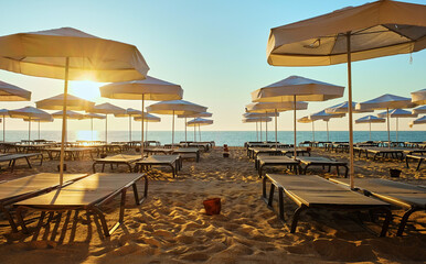 Relaxing on the beach. A row of white beach chairs and umbrellas on a sandy beach at sunrise.