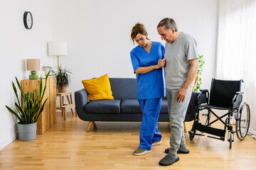 Young adult nursing home helping older man to move at domestic room. Medical female worker in medical uniform supporting senior adult man wheelchair.