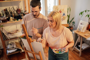 Focused couple painting together at creative art studio and bonding.