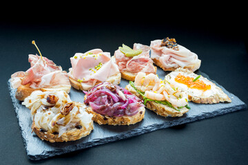 Close-up of typical Venetian cicchetti with different kinds of fillings on a piece of stone on a dark background