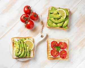 Variation of healthy breakfast toasts with avocado and cherry tomatoes on white wooden background. Food concept.