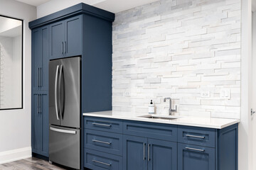 A luxury kitchen detail with blue cabinets, a white marble countertop, polished chrome faucet, and a white tiled stone backsplash.