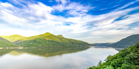 serene lakeside view, with the calm water reflecting the surrounding green mountains and the sky...