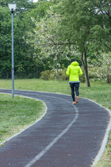 A solitary jogger in a bright yellow jacket and black pants is c, surrounded by greenery and blossoming trees