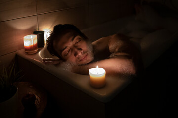 Handsome man bathing in the candlelight. Self care and spa concept	