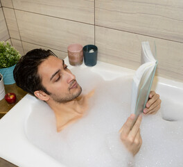 Handsome man lying and relaxing in the bathtub. Young guy bathing in the bathroom. Skin care...