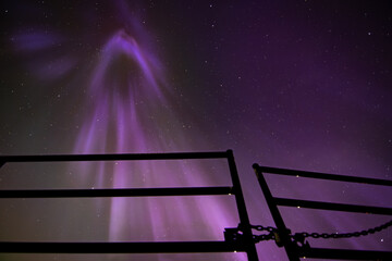Northern Lights dropping from night sky with metal gate silhouette during a level five solar flare...