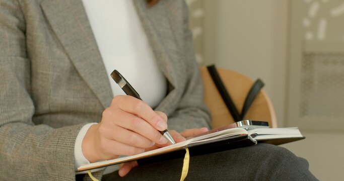 Close-up of female hand takes notes on paper. Close-up of pen and paper. Makes written records of progress and insights during online coaching session in cafe. People lifestyle.
