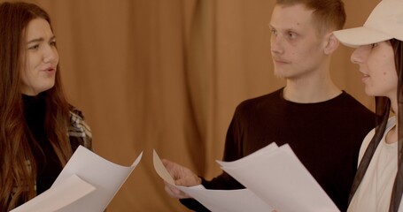 Close-up of students hold scripts in hands, discussing literary readings and reading through roles. This is part of their theater mastery courses. Group of young people talking indoor.
