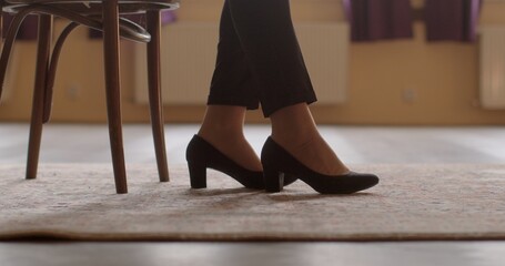 Close-up legs in shoes of seated woman. Focus on her footwear suggests attention to detail and style, reflecting her fashion sense or workplace attire. Woman is dressed elegantly. 