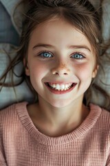 A young girl with blue eyes and a pink sweater is smiling
