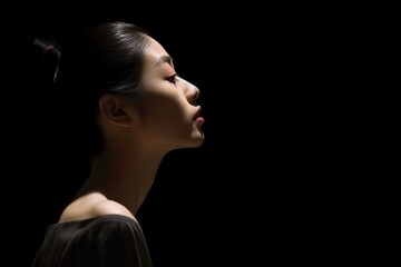 a japanese young woman looks up on isolated black background. a profile of ballerina, her hair pulled into a bun. the concept of hope, mental health, copy space